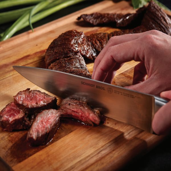 A hand slices a medium-rare steak on a wooden cutting board with a silver knife.