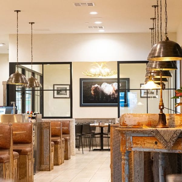 The Hub restaurant interior with rustic wooden booths, industrial pendant lights, and a large cow painting.