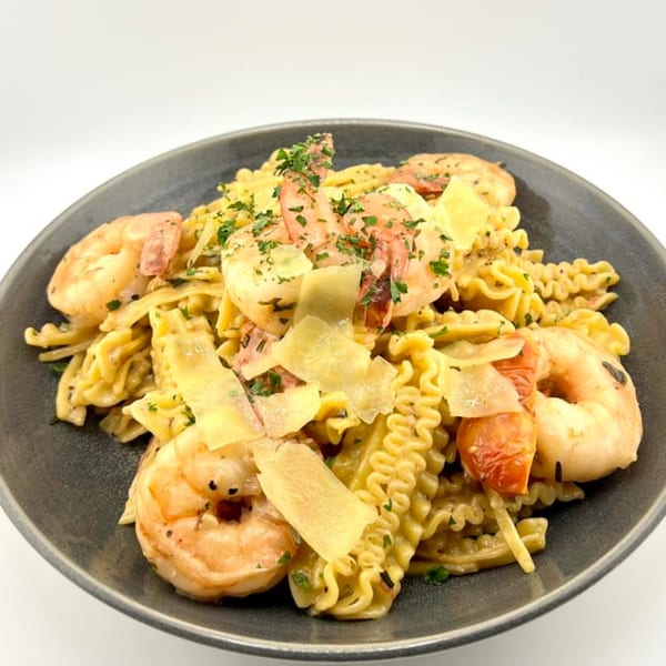 The Hub's shrimp pasta with cherry tomatoes, parmesan, and parsley on a dark plate.