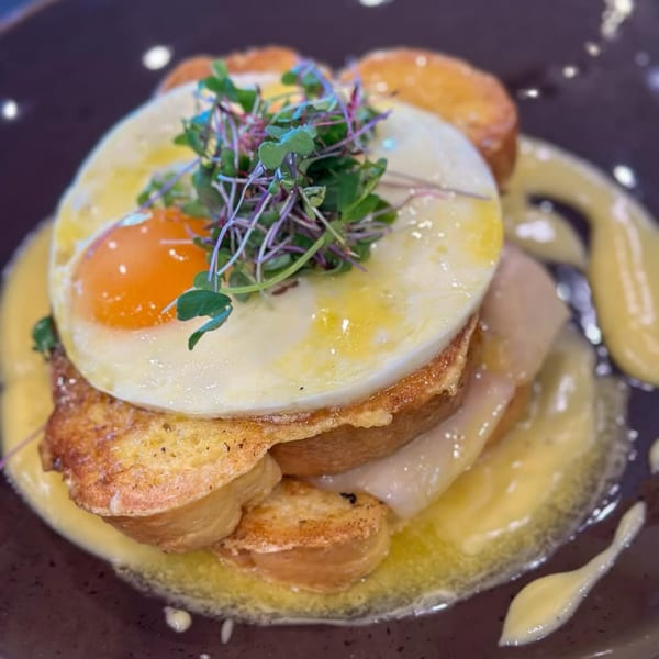 The Hub's American breakfast dish with fried egg, microgreens, and toast, drizzled with sauce.